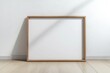 © Salander Studio - a mockup of a blank wooden picture frame on a wooden floor leaning against a white wall - art mock-up template