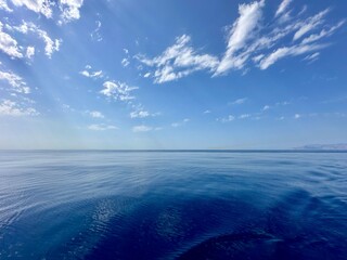 White clouds in the blue sky over a water. Reflection of white clouds and blue sky clouds in the water. Atmospheric natural background.