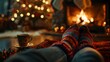 © decorator - Cozy winter scene  close up of woolen socks by a glowing fireplace with a woman enjoying a drink