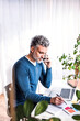 © Halfpoint - Man phone calling and writing notes in planner, working at desk from home. Telecommuting and home office.