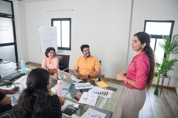 Young indian woman at office discussing about business growth to team members or colleagues in meeting. Start up, leadership, presentation and workplace communication concept.