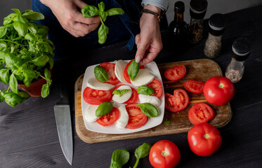 Woman Decorates Caprese Salad With Basil, Made From Tomatoes And Mozzarella Cheese. Top view