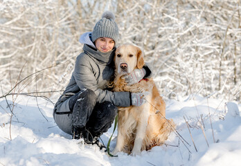 Wall Mural - Teenage Girl And Golden Retriever Sit Together In Snow-Covered Forest During Winter