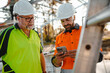 © Austockphoto - Two men wearing safety gears on the site with one holding a mobile device focus on phone