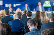 © Anton Gvozdikov - Business professionals attending a conference with a panel of speakers on stage discussing various topics.