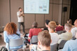 © Anton Gvozdikov - Group of people attending seminar, focusing on speaker presenting at front of conference room with projector screen.
