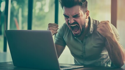 A man celebrates his success with a loud yell and clenched fists, looking at his computer screen.