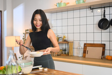 Wall Mural - Beautiful young woman in activewear preparing a nutritious breakfast or snack at kitchen counter