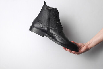 Wall Mural - Hand holding black brogue boot on gray background