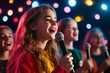 © woters - Young girls joyfully singing together on stage under colorful lights during a musical performance at an event