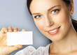 © vgstudio - Closeup portrait of smiling woman showing white blank mockup mock up empty businesscard plastic credit card, with blank copy space, isolated grey background. Brunette female model at studio image.