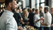 © Anna - A well-dressed man smiles while holding a glass of wine, surrounded by a group of people mingling and enjoying appetizers at a vibrant indoor gathering