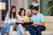 © StockImageFactory - Happy Indian family of four relaxing on a sofa, reading books Or viewing photo album together
