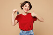 © ViDi Studio - Young smiling happy woman she wear red t-shirt casual clothes hold in hand car key fob keyless system show thumb up isolated on plain pastel light beige background studio portrait. Lifestyle concept.