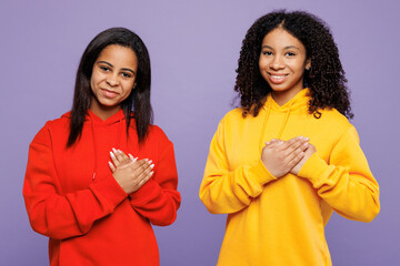 Wall Mural - Two young smiling little kid teen girls women they wear red yellow hoodie casual clothes put folded hands on heart looking camera isolated on plain pastel light purple background. Lifestyle concept.