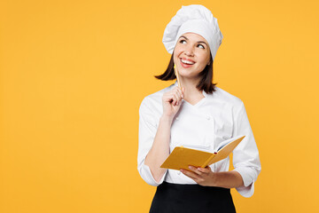 Wall Mural - Young minded chef cook baker woman wear white shirt black apron uniform toque chefs hat hold in hand book reading recipe prop up chin think isolated on plain yellow background. Cooking food concept.