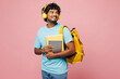 © ViDi Studio - Young Indian boy student wears blue t-shirt casual clothes backpack bag hold books listen to music in headphones look aside isolated on plain pink background. High school university college concept.