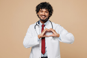 Wall Mural - Young Indian doctor man wear white medical gown suit work in hospital clinic office show shape heart with hands heart-shape sign isolated on plain beige background studio. Healthcare medicine concept.