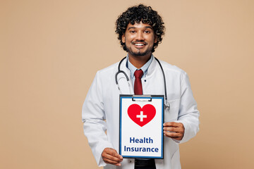 Wall Mural - Young Indian doctor man wear white medical gown suit work in hospital clinic office hold clipboard with health insurance document isolated on plain beige background studio Healthcare medicine concept