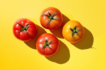 Wall Mural - Four tomatoes are sitting on a yellow surface. The tomatoes are red and orange in color. The image has a warm and inviting mood