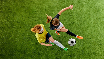 Two athletic women, locked in fierce duel over ball, showcasing agility and skill, each fighting for dominance on soccer field. Aerial view. Concept of sport, competition, tournament, games, event.