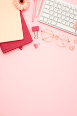 Wall Mural - Office desk table with computer keyboard, glasses, paper notebooks, supplies, flowers on pink background. Top view with copy space. Flat lay