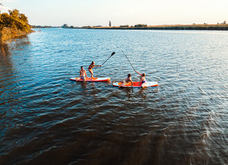 Wall Mural - Aerial view of friends on sup board enjoying a day at lake during sunset.