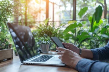 Wall Mural - The business woman sits at her office table while she works online on her laptop computer while using her mobile phone