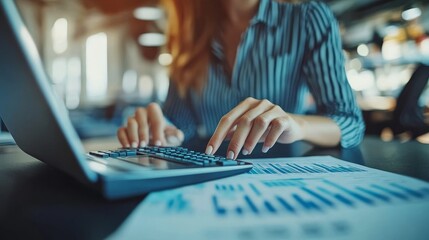 Canvas Print - In a business room, an office worker works at a calculator to calculate financial reports and sales data on a laptop computer with business documents on an office table. Business, finance, and