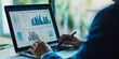© kwanchaift - Corporate accountant reviewing financial statements on a laptop detailed charts and precise figures modern digital interface