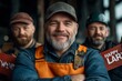 © Kakabe - Three bearded men in work attire, one wearing an orange apron and smiling confidently, perfect for themes of teamwork in craftsmanship, manual labor pride, and camaraderie in the workplace,