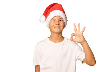 Portrait of a smiling boy in a red hat and white t-shirt with okay sign gesture on a transparent background. A child in a Christmas hat of Santa Claus.