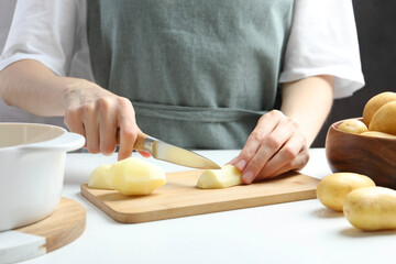 Poster - Woman cutting raw potato at white table, closeup