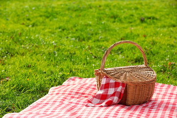 Wall Mural - One picnic wicker basket with checkered napkin and blanket on green grass. Space for text