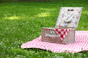 Wall Mural - One picnic wicker basket with checkered napkin, tableware and blanket on green grass. Space for text