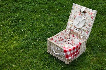 Wall Mural - One picnic wicker basket with checkered napkin and tableware on green grass. Space for text