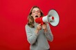 © яна винникова - Young woman passionately shouting into a red megaphone against a bright red background during an advocacy campaign