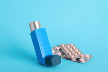 Inhaler and pills on light blue background, closeup. Asthma treatment