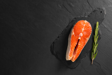 Canvas Print - Fresh salmon steak and rosemary on dark textured table, top view. Space for text