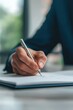 © Jammy - A focused hand writing in a notebook with a silver pen, capturing the essence of productivity and organization in an office setting.