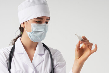 Doctor wearing face mask looking at measurement on medical thermometer over white background 