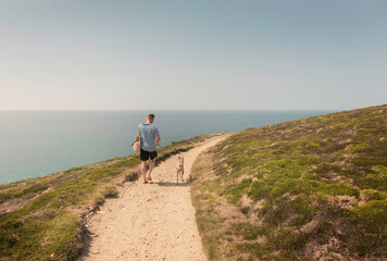 caucasian casual attire man walking whippet dog along clifftop coastal path towards bedruthan steps 