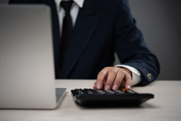 Wall Mural - Businessman using a calculator alongside a laptop for financial analysis and budgeting tasks. Represents accounting, financial planning, and data analysis in a corporate setting.