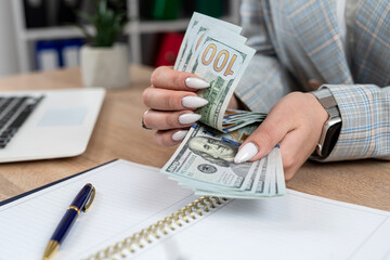 Canvas Print - Paper dollar bills in the female hands and laptop empty notepad at office desk