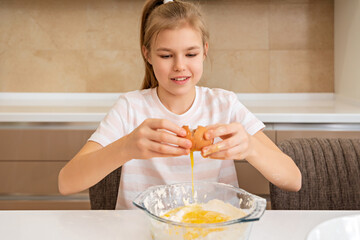 Preteen girl breaks an egg in a bowl on a table, cooking in kitchen