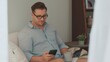 © InfiniteFlow - Middle age man sit on sofa with coffee cup in room using phone search data for occupation, raising children to be good adult or entertainment. Businessman use technology for convenience. Divergence.