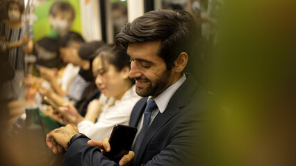 Wall Mural - Smiling caucasian business man looking at mobile phone or playing social media while sitting in train. Attractive project manager going to work place by using public transport in rush hour. Exultant.