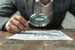 © Vera - photo of a person in a suit using a magnifying glass to examine financial documents related to a business fraud investigation.