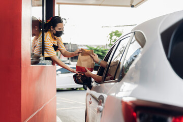 Hand Man in car receiving coffee in drive thru fast food restaurant. Staff serving takeaway order for driver in delivery window. Drive through and takeaway for buy fast food for protect covid19.