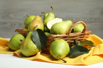 Wall Mural - Fresh green pears with leaves and basket on white table, closeup